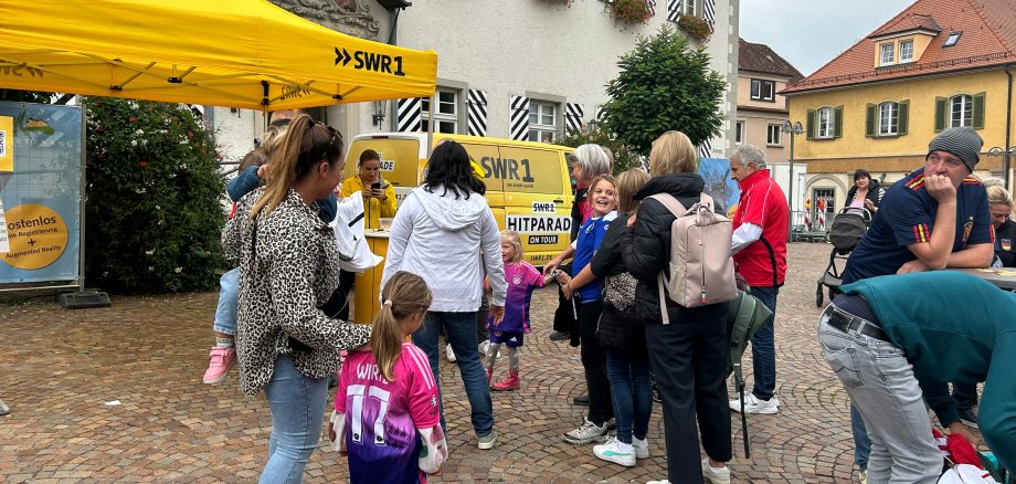 Menschen warten in einer Schlage vor dem SWR1-Baldachin auf das Zählen ihrer Sporttrikots